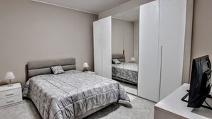 Ein Schlafzimmer mit Bett, Nachttisch, Lampe, Kleiderschrank und Fernseher.