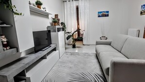 Ein modernes Wohnzimmer mit grauem Sofa, Flachbildfernseher und einer Zimmerpflanze.