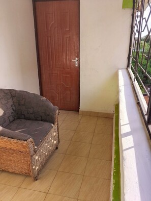 Ein Balkon mit einem Korbsessel, einer Holztür und einem Metallgeländer.