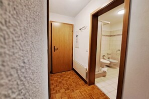 Kapea käytävä, jossa on puinen ovi, joka johtaa kylpyhuoneeseen, jossa on wc, bidee ja pesuallas.