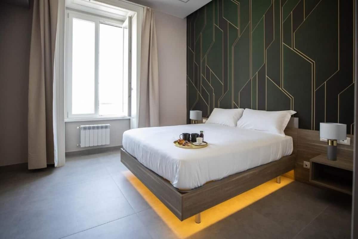 Une chambre d’hôtel moderne avec un grand lit, des lampes de chevet, une fenêtre avec des rideaux et un mur orné d’un motif géométrique.