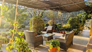 An outdoor patio with wicker furniture, potted plants, and a pergola structure. - Chestnut Apartment Four Poster (Vélez-Rubio)