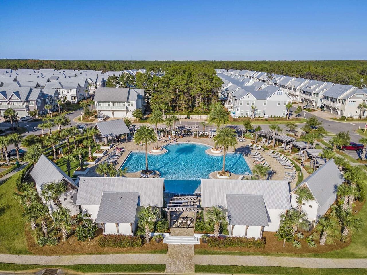 A resort with multiple buildings, a central swimming pool, and surrounding palm trees.