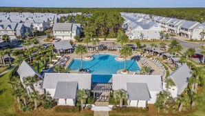 Ett semesterområde med flera byggnader, en central pool och palmer som omger området.