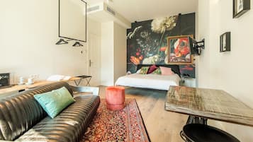 Una habitación de hotel moderna con un sofá, una mesita, una cama con ropa de cama colorida, una gran obra de arte floral en la pared y un espejo.