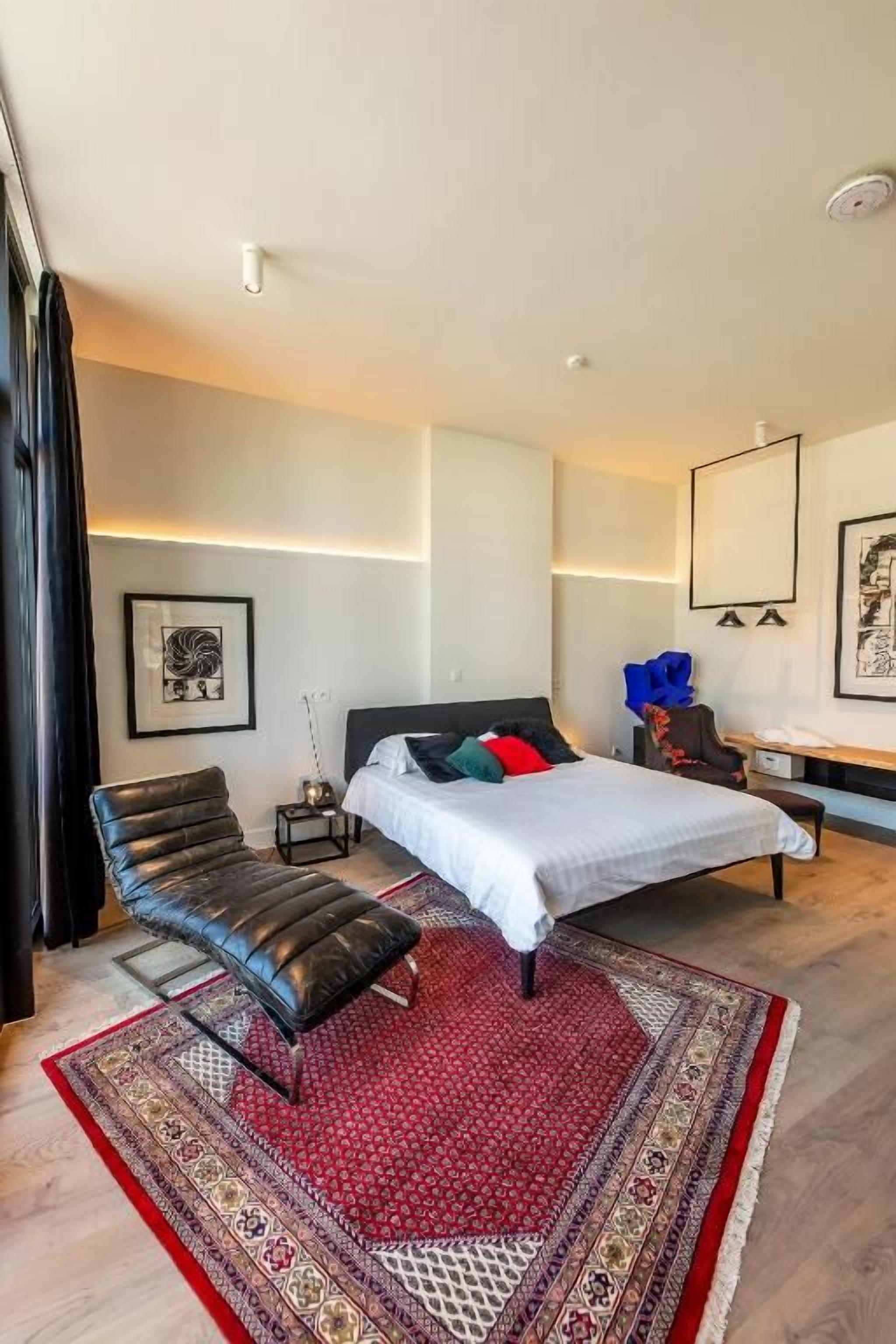 Une chambre à coucher moderne avec un lit, une chaise, une table de chevet et un tapis.