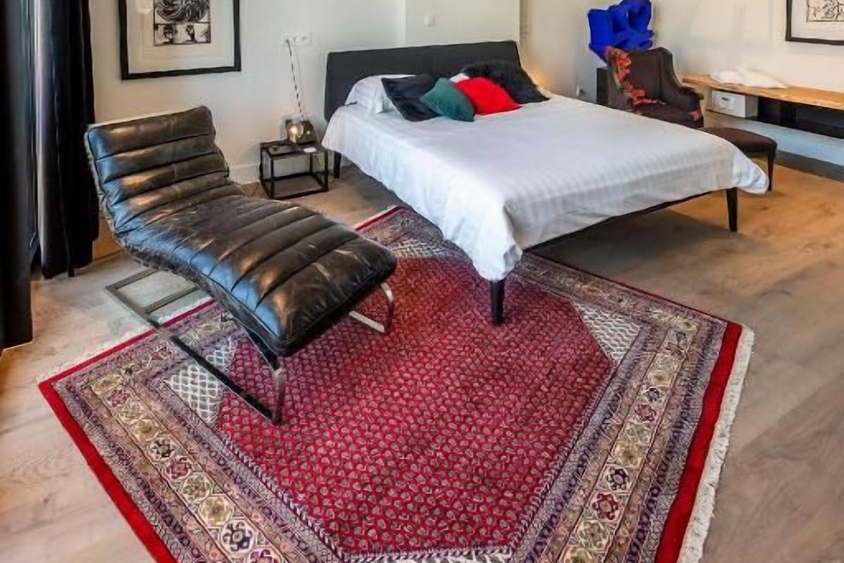 A modern bedroom with a bed, a chair, a bedside table, and a rug.