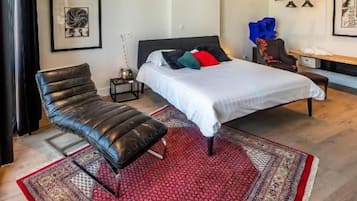 A modern bedroom with a bed, a chair, a bedside table, and a rug.