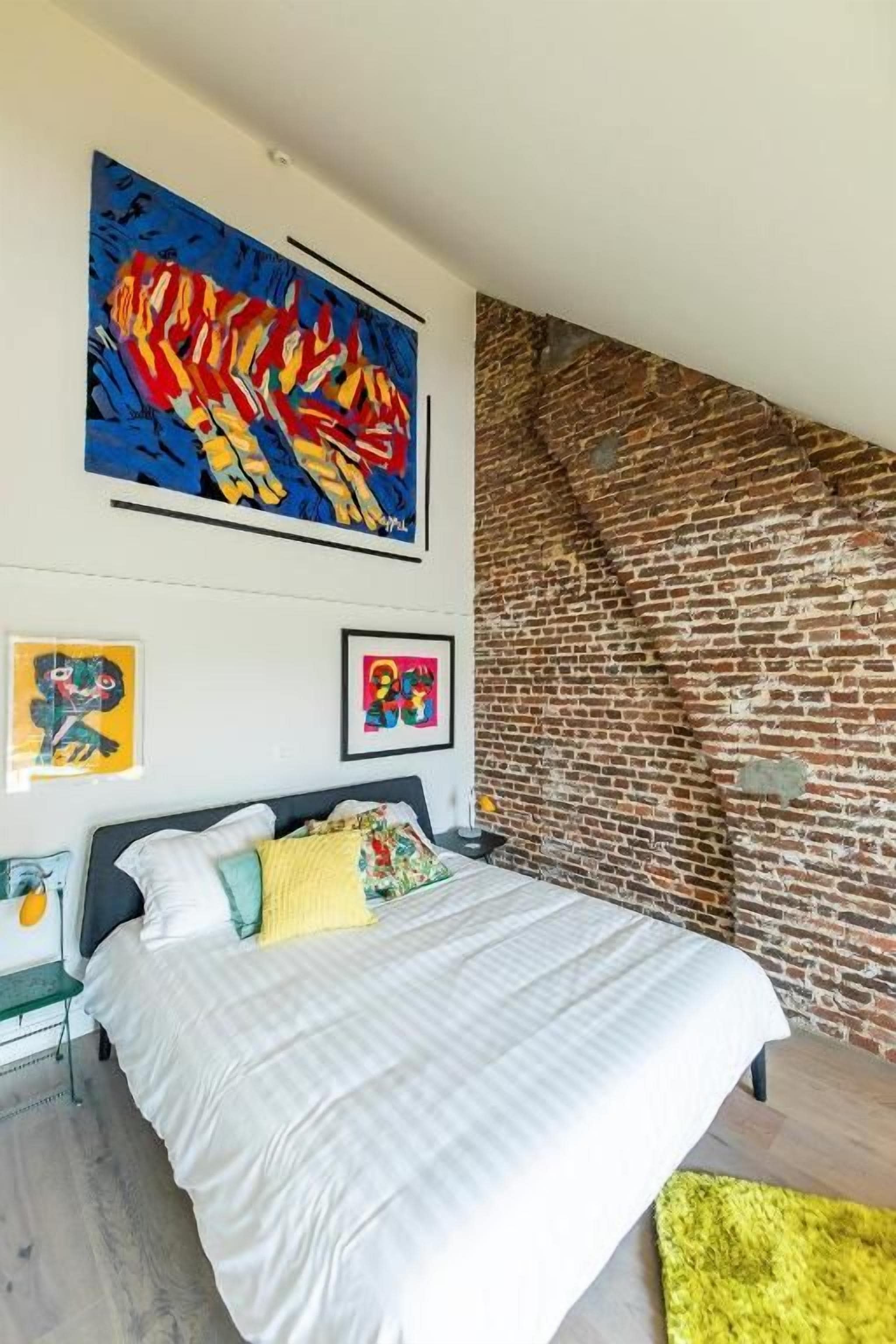A bedroom with a bed, a brick wall, and two framed artworks.