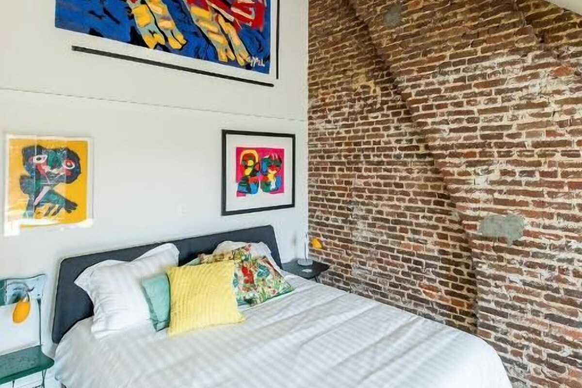 A bedroom with a bed, a brick wall, and two framed artworks.