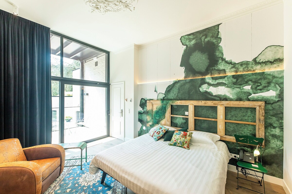 A bedroom with a large bed, a chair, a desk, and a view of the outdoors.