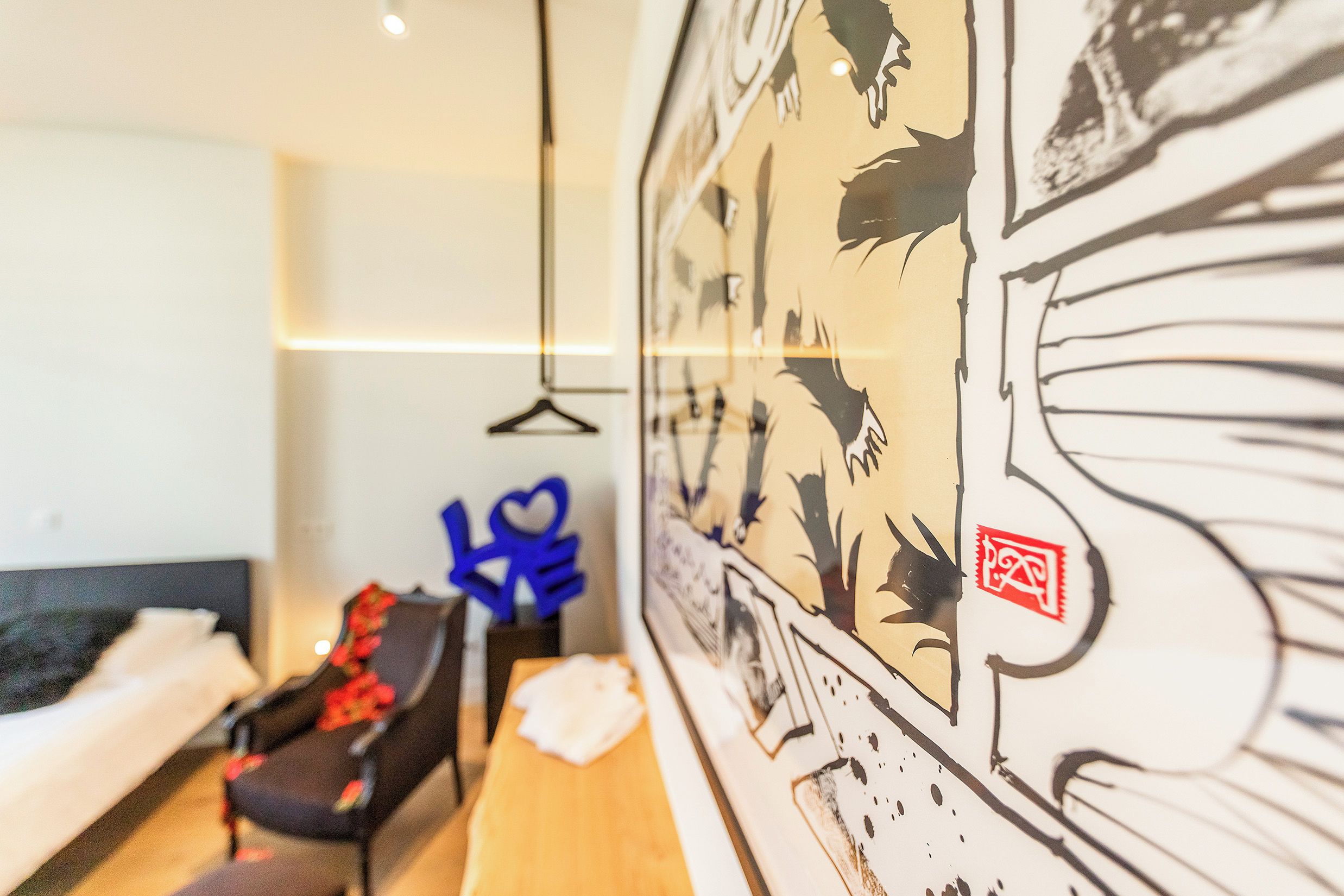 Habitación de hotel con cama, sofá, lámpara colgante y pared con un mural grande.