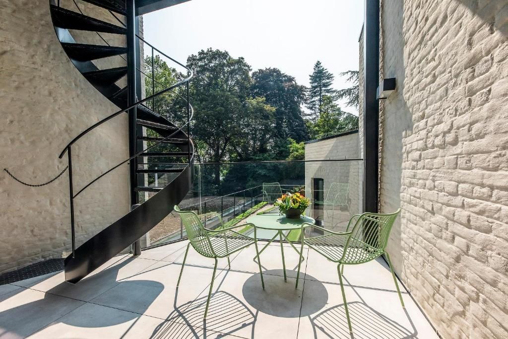 Un espacio exterior moderno con una escalera de caracol, una partición de vidrio y una mesa con sillas.