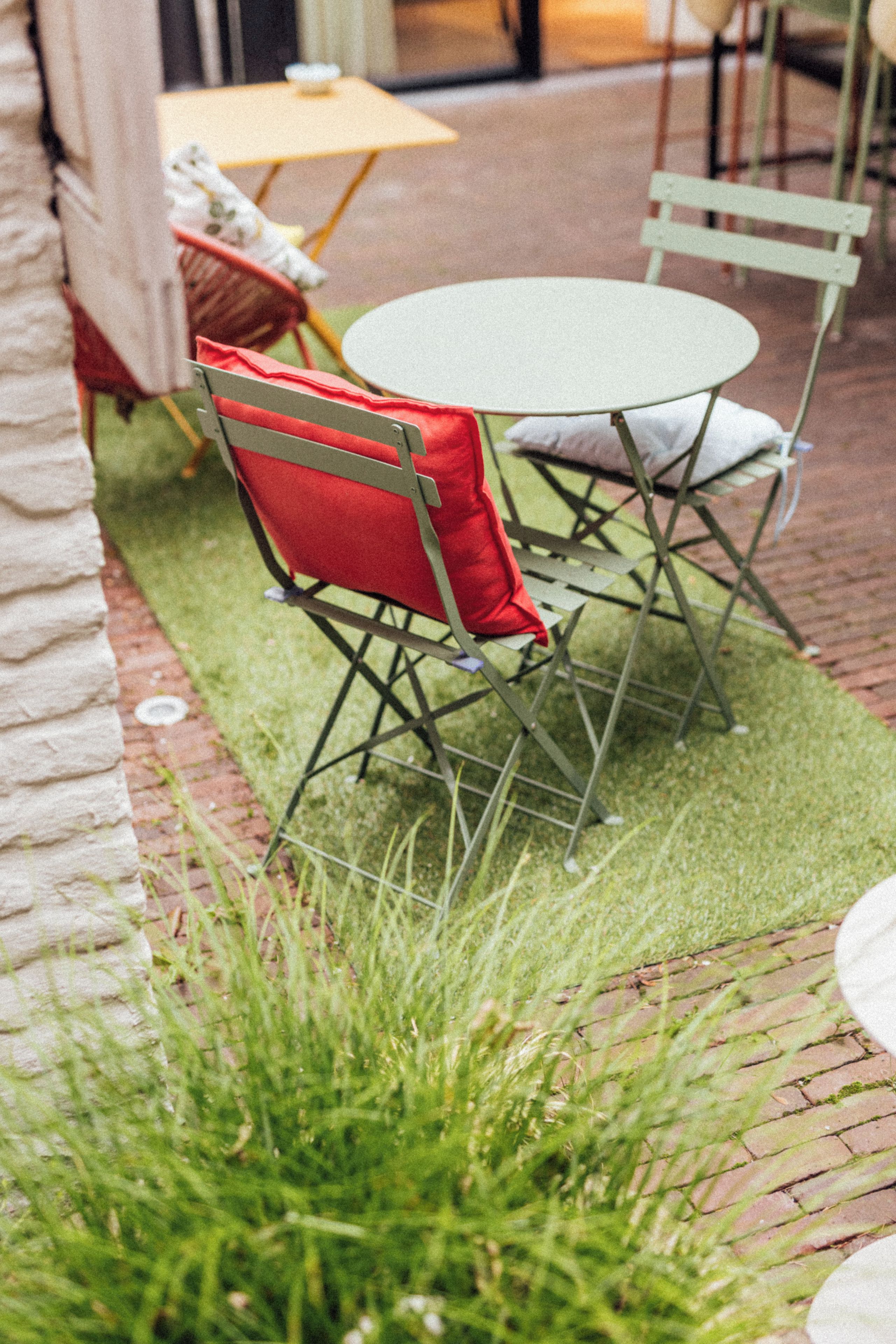 Een terras met een ronde tafel en twee stoelen, waarvan er één een rode kussen heeft.