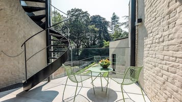 A modern outdoor seating area with a spiral staircase, a glass balustrade, and a view of trees.