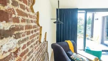 A room with a brick wall, a black sofa, a yellow throw, and a view through a window.