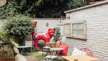 Un patio con piso de ladrillo, mobiliario exterior y una escultura roja.