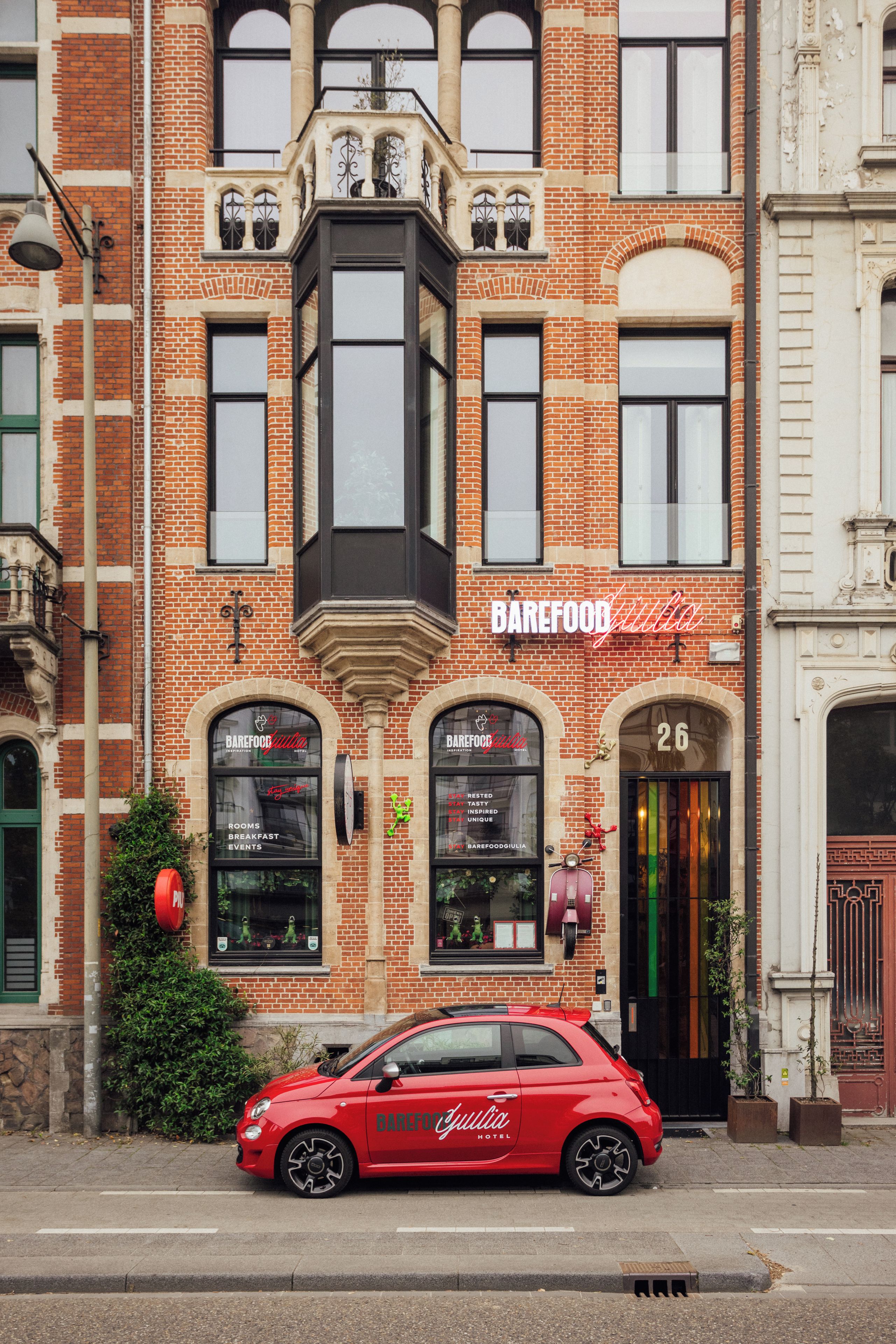 Une voiture rouge est garée devant un immeuble sur lequel on peut lire l’inscription « Barefoot Giulia Hotel ».