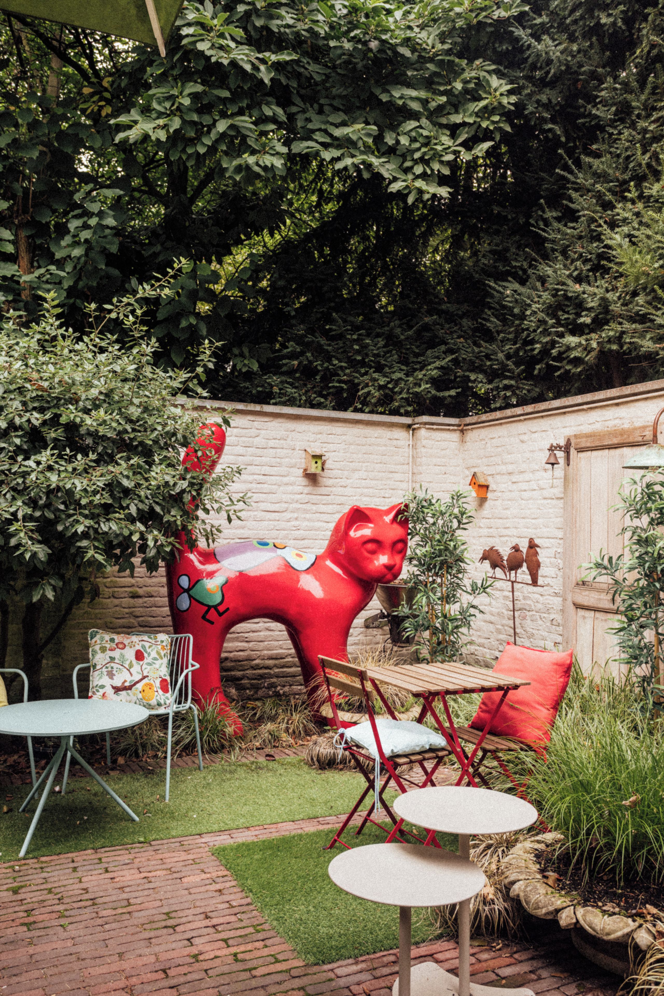 A garden with a red cat sculpture, a brick wall, and outdoor furniture.