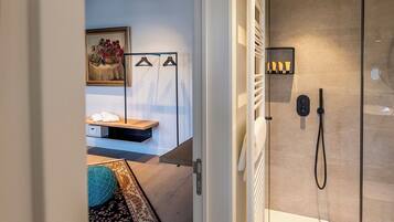 A modern bathroom with a glass shower enclosure, a towel rack, and a small shelf with toiletries.