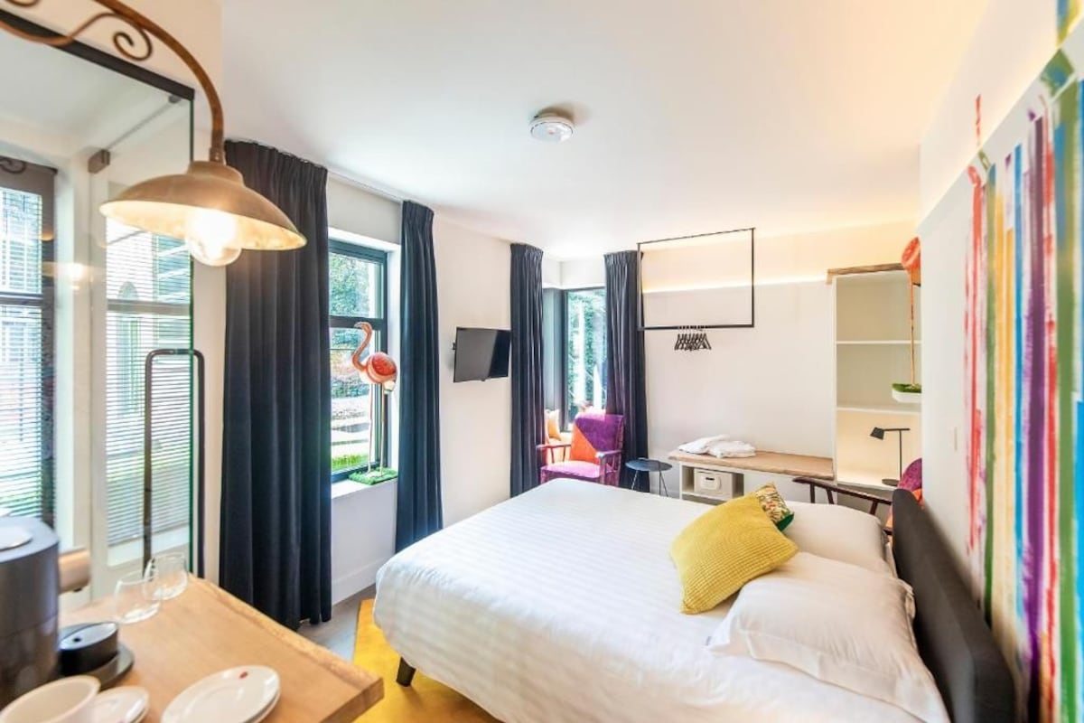 Una habitación de hotel con cama, escritorio con silla, televisor y ventana con cortinas.