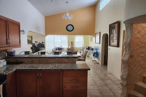 A kitchen with a granite countertop, wooden cabinets, a chandelier, and a clock on the wall.