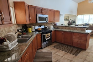 A kitchen with wooden cabinets, a stainless steel microwave, a stove, and a granite countertop. - Anguilla Vacation Home – Cradle Grove (Little Harbour)