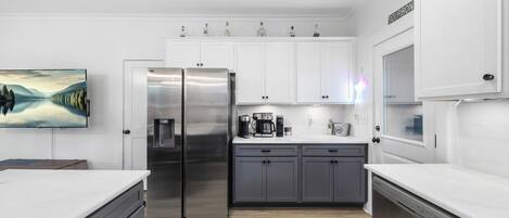 A modern kitchen with white cabinets, stainless steel appliances, and a flat-screen TV.