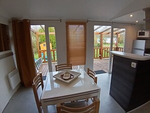 Eine kompakte Küche mit Essbereich, einem kleinen Kühlschrank und Blick auf eine Holzterrasse und einen Garten.