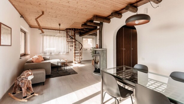 A modern living room with a glass dining table, a sofa, a rocking horse, and a spiral staircase.