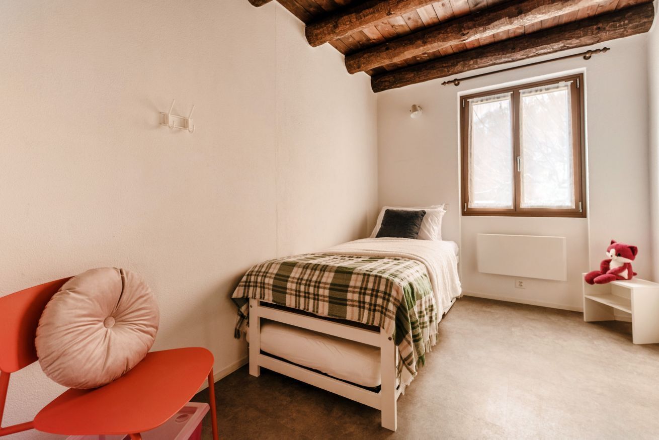 A bedroom with a bed, a chair, a window, and a teddy bear.