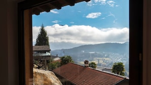 A view through a window of a building with a tiled roof, a stone wall, and a view of a town with mountains in the distance.