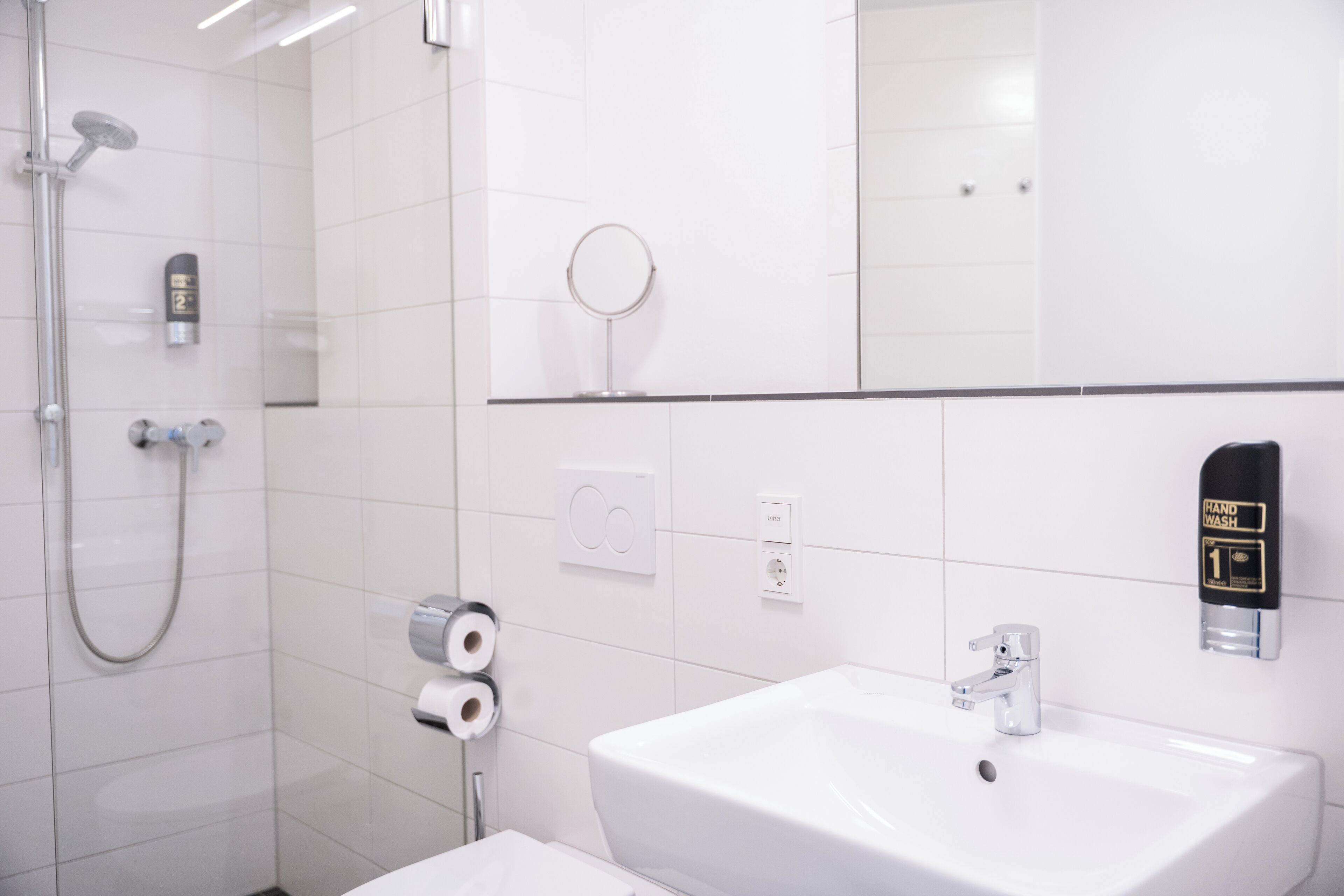 Un bagno moderno con doccia, carta igienica, erogatore di sapone e lavabo.