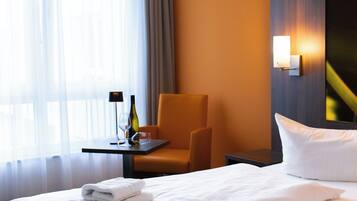 Habitación de hotel con dos camas, una silla, una mesita con una botella y un vaso, y una lámpara fijada a la pared.