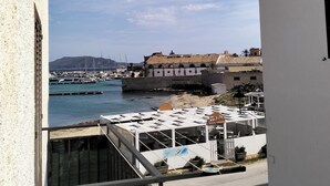 Vista sul litorale da un balcone che si affaccia su una marina con barche, un edificio storico e cielo sereno.
