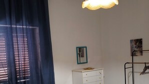 Una stanza con una cassettiera bianca, un tappeto a righe, una lampada a sospensione e un appendiabiti.
