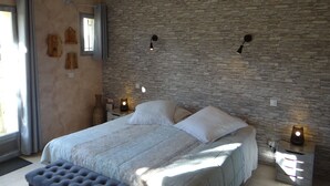 Ein Schlafzimmer mit Steinwand, einem Bett mit weißer Bettwäsche, einer Bank und zwei Nachttischen mit Lampen.