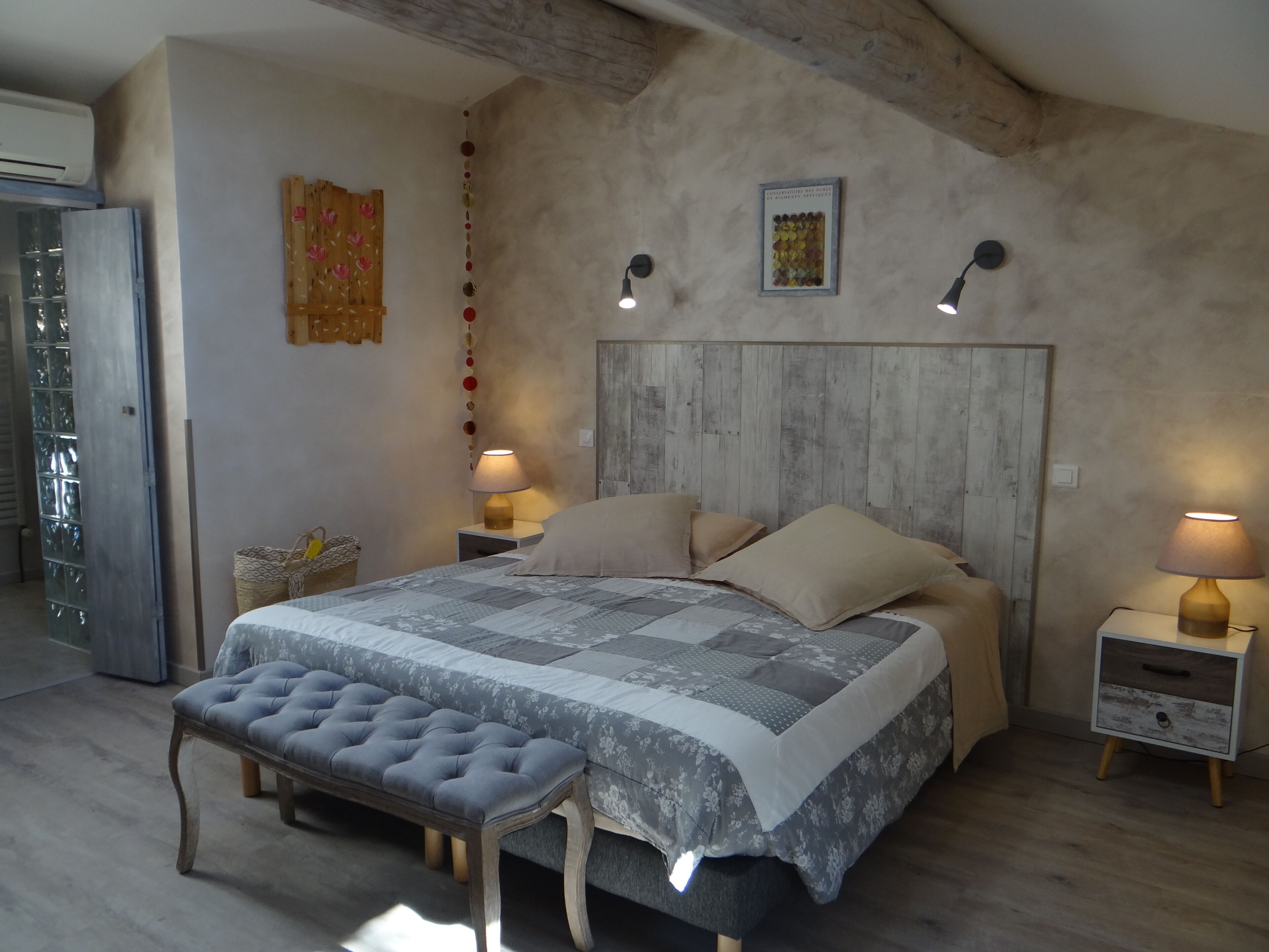 A bedroom with a large bed, two bedside lamps, a bench, and a wooden headboard.