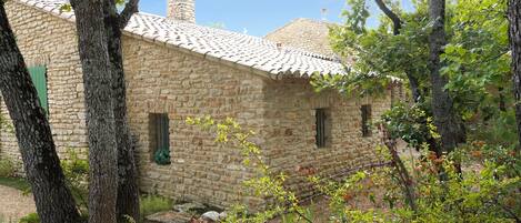 A stone building with a tiled roof, surrounded by trees and a garden.