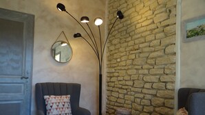 Ein Wohnzimmer mit Steinwand, einem runden Spiegel, einer modernen Stehlampe und zwei Sesseln.