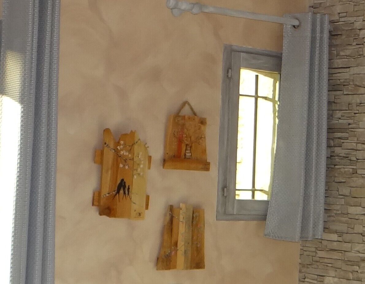 Ein Zimmer mit einer Steinsäule, einem Fenster mit Vorhang und drei Holzarbeiten an der Wand.