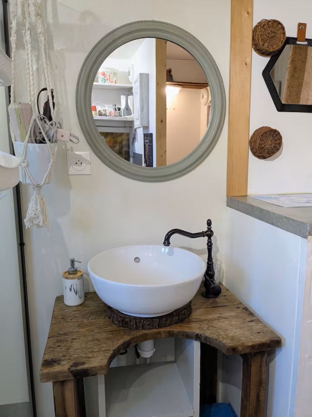 A bathroom with a round mirror, a white sink, and a wooden vanity.