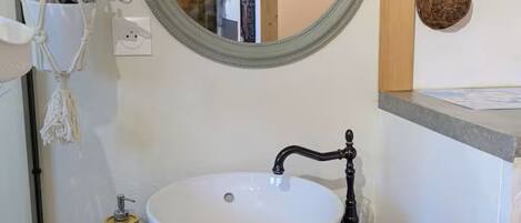 A bathroom with a round mirror, a white sink, and a wooden vanity.