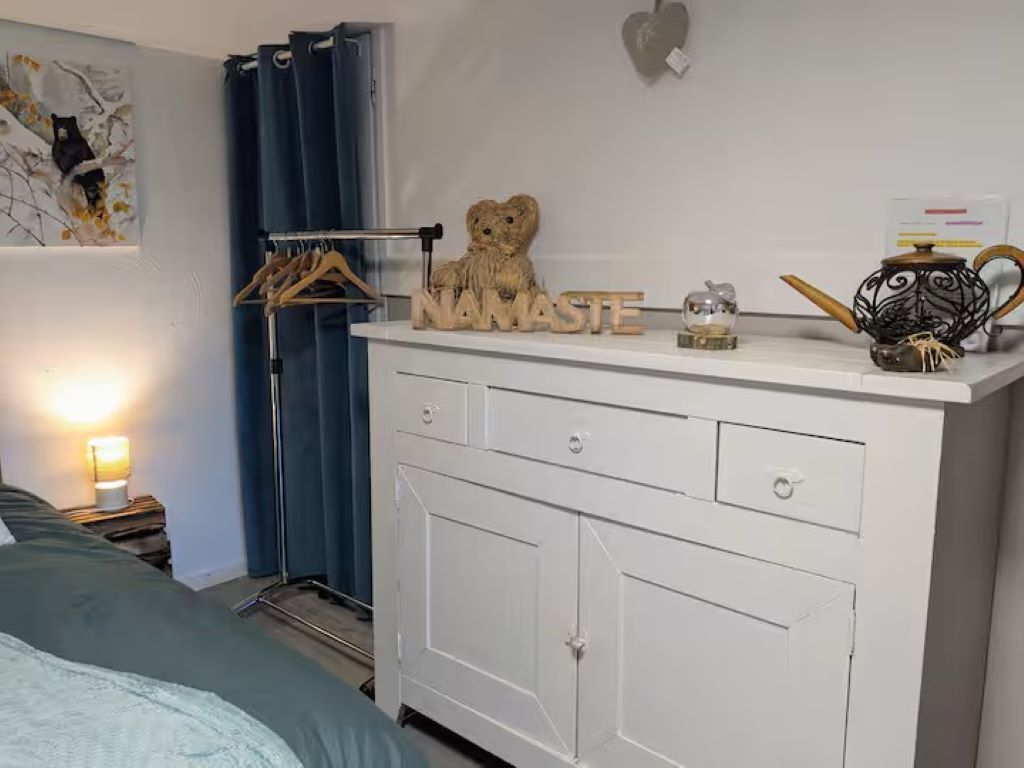 A bedroom with a bed, a dresser with a mirror, a hanging light, and a wall decoration.