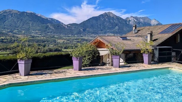 Ein Schwimmbad mit Bergblick, ein Gebäude mit Satteldach und Kübelpflanzen.