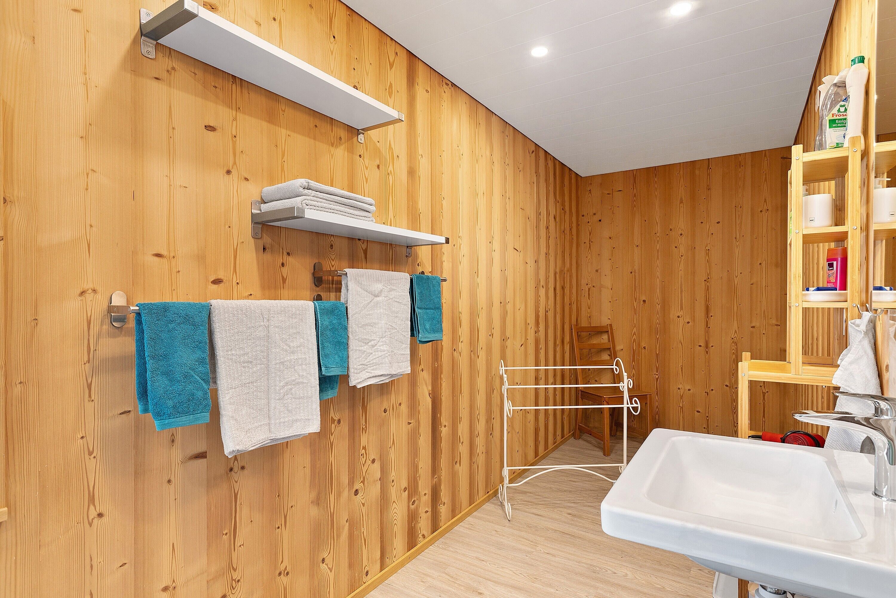 A wooden-paneled bathroom with a white sink, towel racks, and a drying rack.