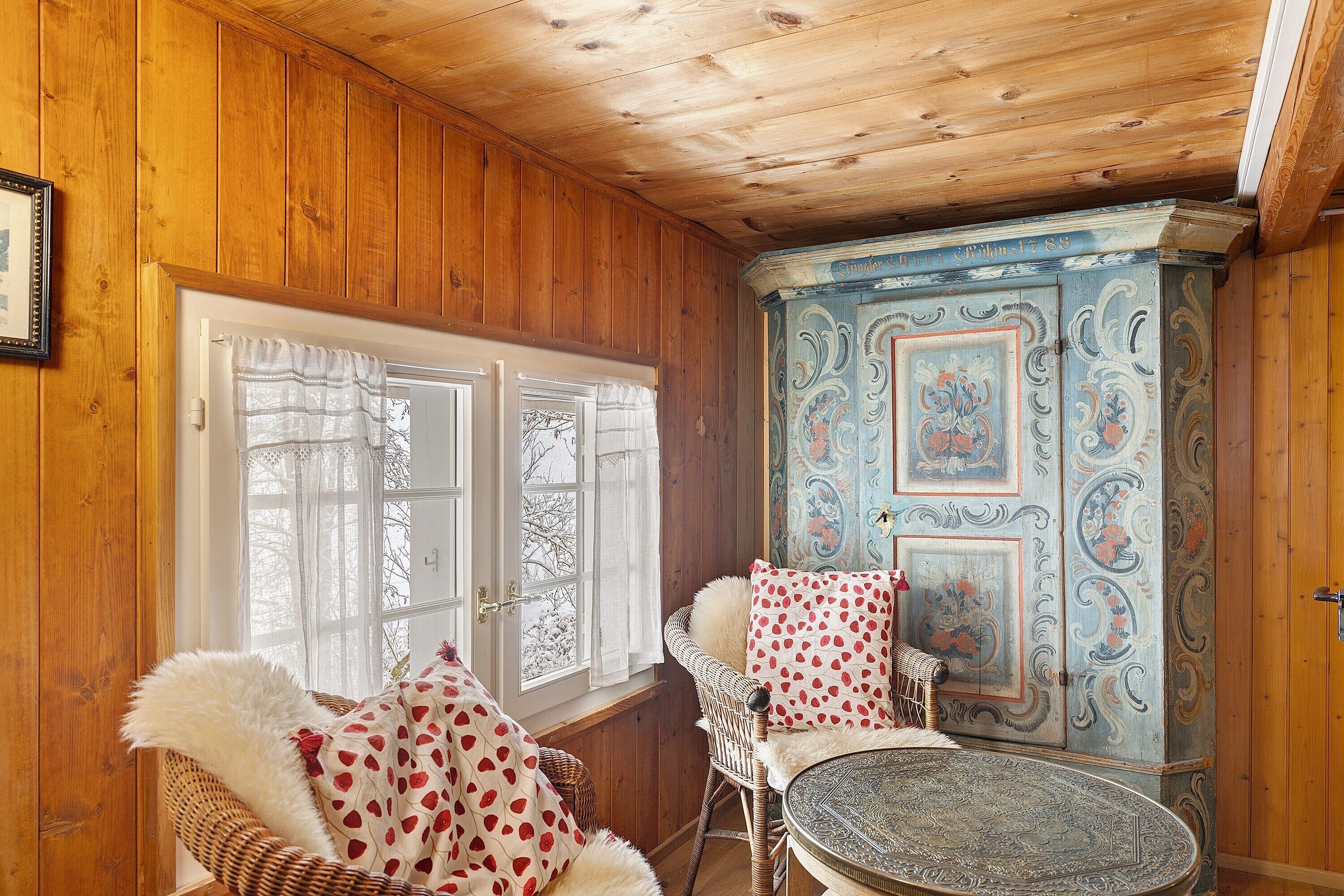 A wooden-paneled room with a wicker chair, a round table, and a decorative cabinet.