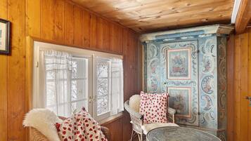 A wooden-paneled room with a wicker chair, a round table, and a decorative cabinet.