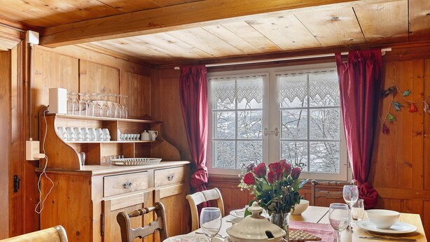 L’intérieur d’un chalet en bois comprend une table à manger pour quatre personnes, un coin cuisine avec des étagères et une fenêtre avec des rideaux.