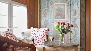 Une pièce avec un fauteuil en osier, une table ronde ornée d’un vase de fleurs et un mur à motifs.